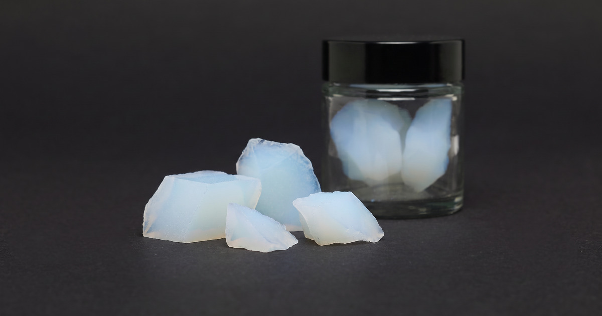 Weihnachtsgeschenke für Nerds: 6 Ideen aus dem Labor 1 Lose Bruchstücke von Silica Aerogel mit blauem Schimmer, dahinter der Glastiegel des Produkts auf dunklem Grund